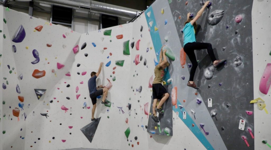 born family climbing boulder walls together