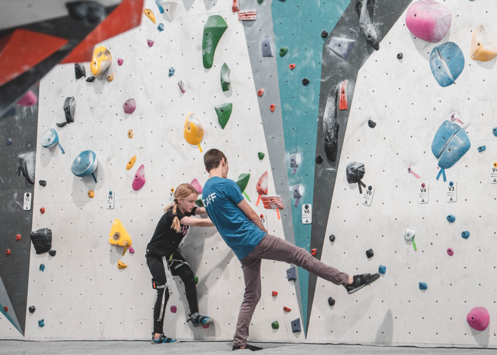 Youth climbing coach helping a young climber on the wall at Alpine