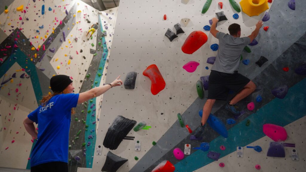 Alpine staff guide coaching a beginner climber on the bouldering wall